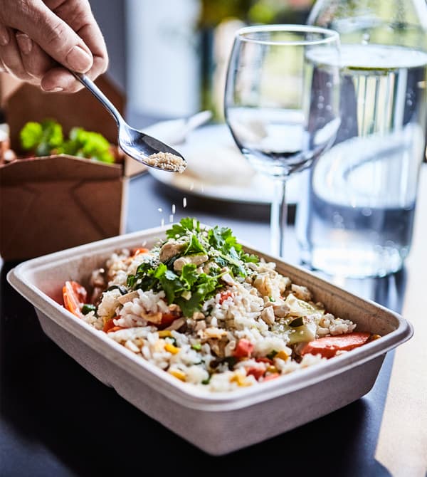 Graines de sésame en train d’être saupoudrées sur du riz sauté dans une boîte.