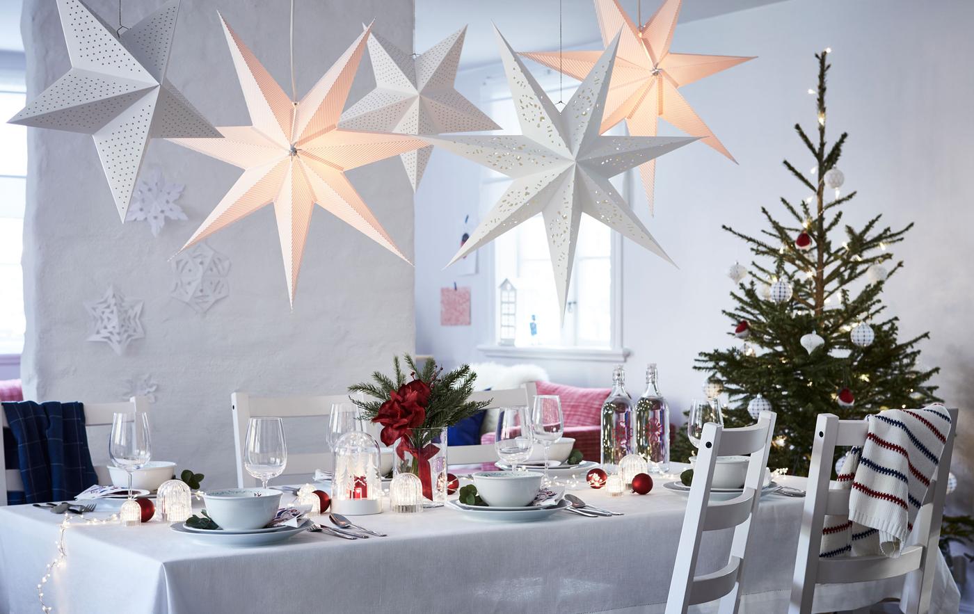 Grande pièce claire, sobrement meublée avec une longue table dressée pour les fêtes. Un arbre de Noël à une extrémité, des étoiles de papier suspendues au plafond.