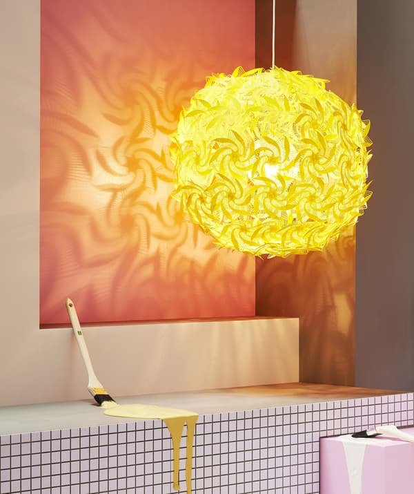 Grande suspension jaune avec motifs découpés, projetant des motifs décoratifs sur un mur rouge.