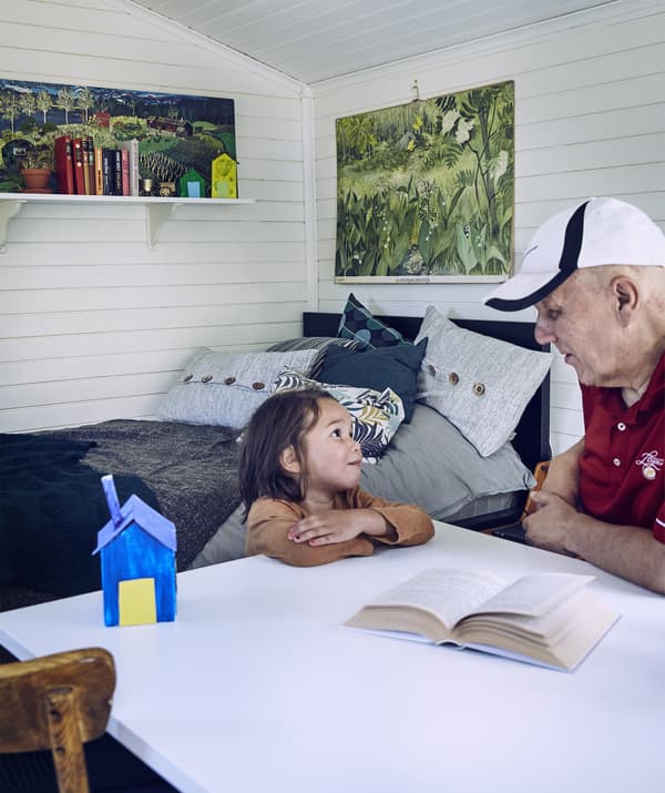 Grandpa and grandson sitting at a fold-out table in a self-contained annex room with white-washed wooden walls, blue bed and wall art.