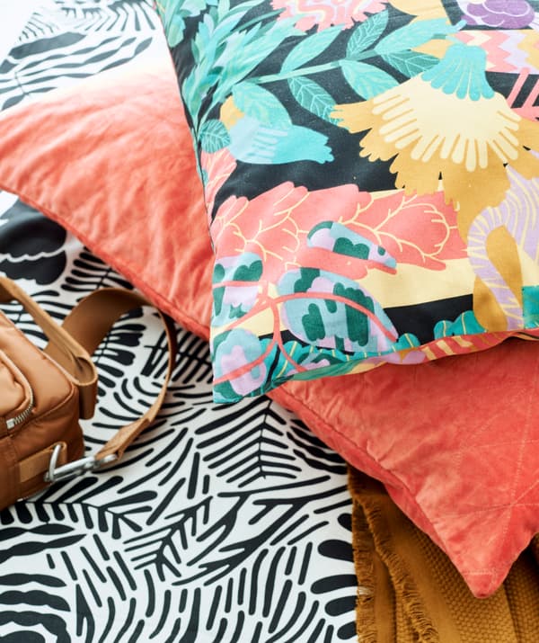 Graphic black and white fabric with one salmon-pink velvet cushion and one multicolored patterned cushion on top.