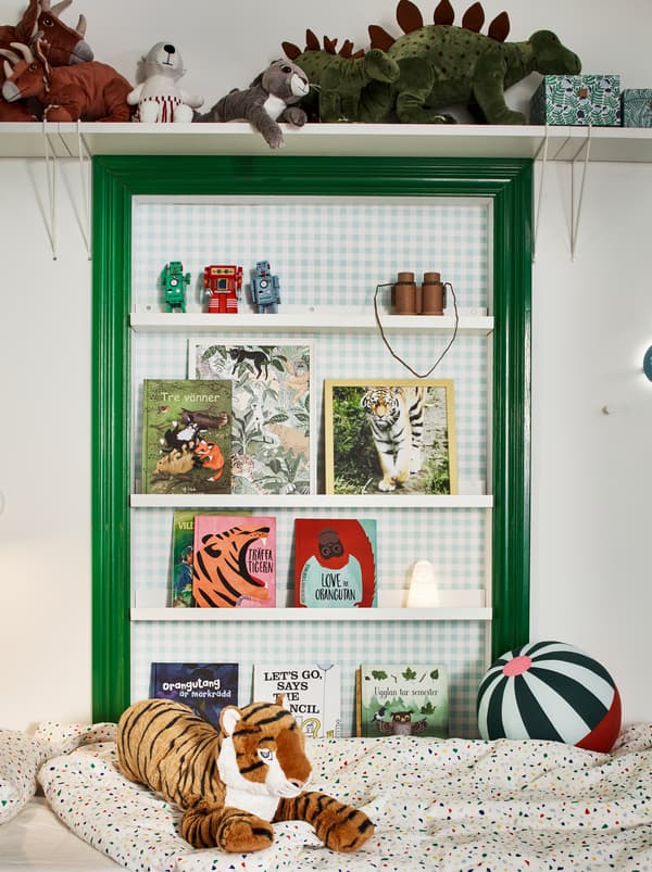 Green and white wall above the bed in a children’s room. Soft toys on a wall shelf and books on MOSSLANDA picture ledges.