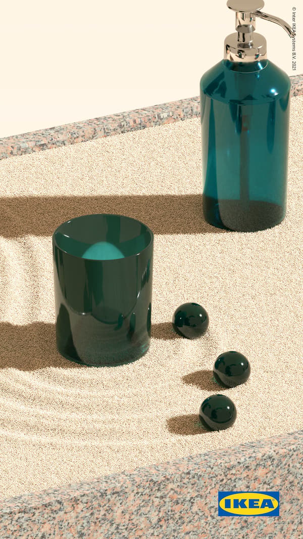 Green-glass SKISSEN soap dispenser and toothbrush holder stand on yellow sand, raked into swirls, before a yellow background.