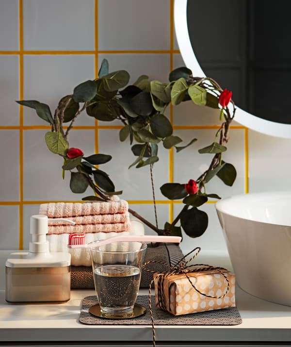 Green IKEA SMYCKA artificial leaf branches shaped like a heart, decorating a bathroom shelf.