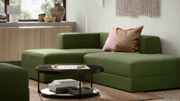 Green JÄTTEBO modular sofa with chaise lounge in a cozy room setup, featuring soft lighting, decorative cushions, and a black circular coffee table.