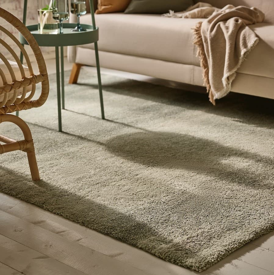 Green medium pile rug shown under a beige sofa, green side table and rattan armchair