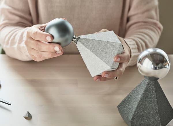 Grey and silver baubles being inserted into the tops of jewel-shaped paper boxes.
