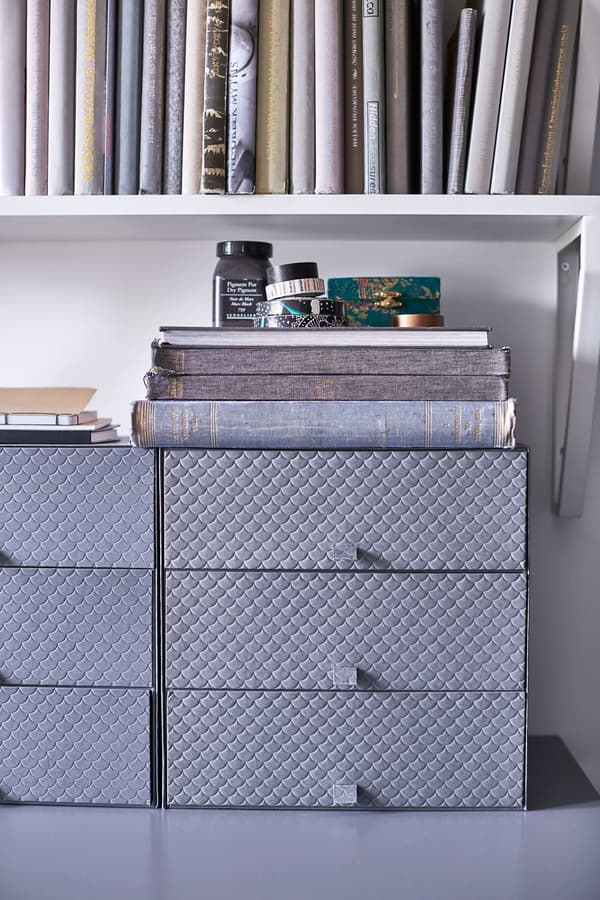 Grey boxes with drawers sit on a desk in a dorm room.