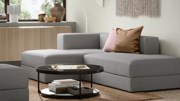 Grey JÄTTEBO modular sofa with chaise lounge in a minimalist space, complemented by neutral decor and a black round coffee table with books.