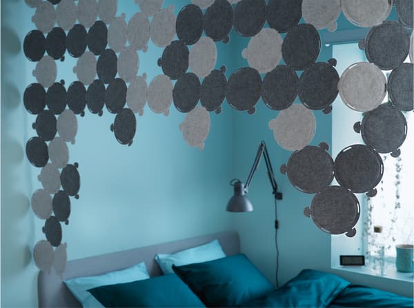 Grey sound absorbing panels are mounted in the ceiling and surround a bed in a blue and green bedroom.