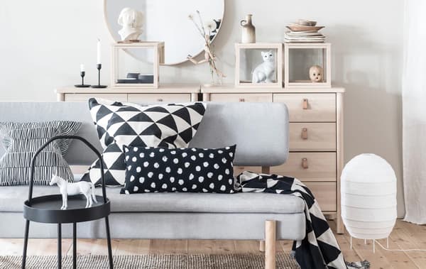 Grey YPPERLIG sleeper sofa with black and white textiles in a living room with natural wood drawers and minimal decor.