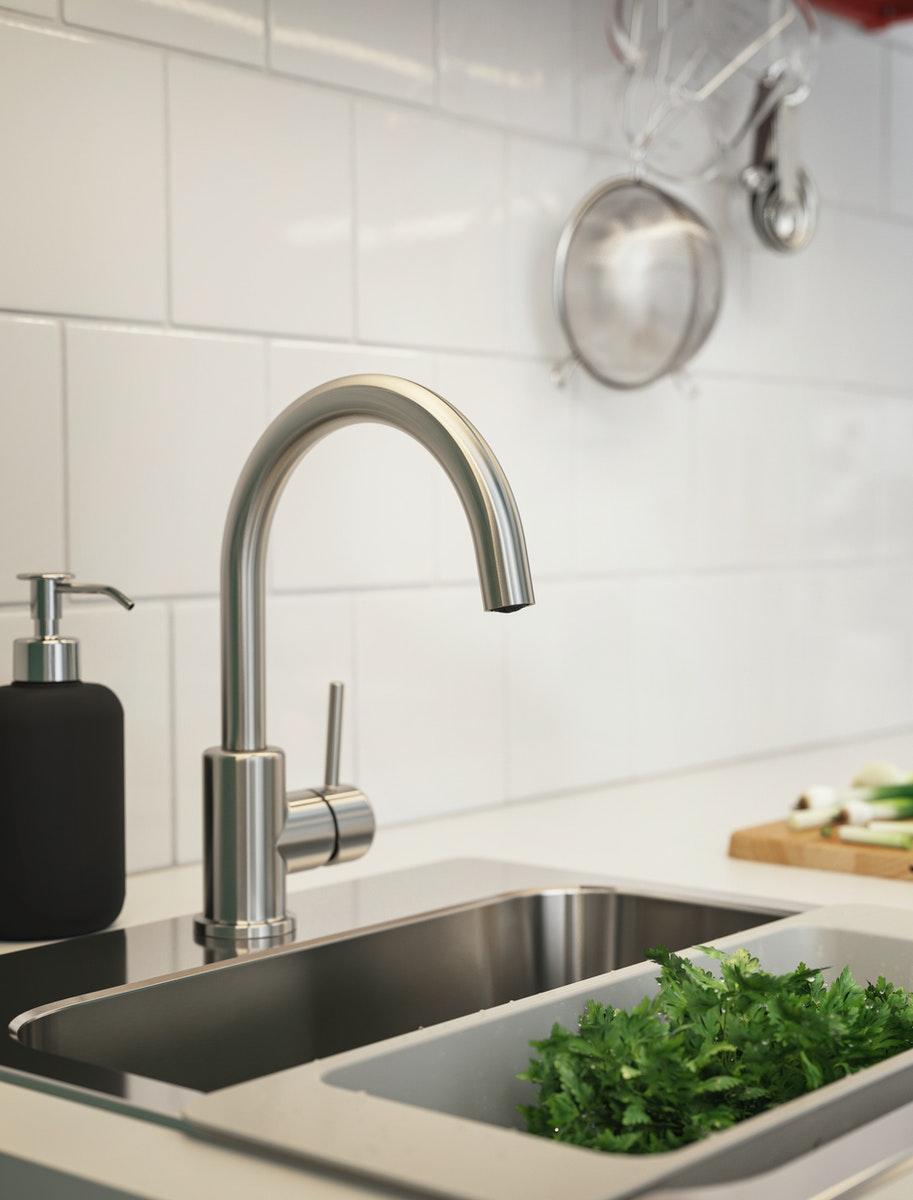 Grifo de cocina metálico GLYPEN, junto a un colador blanco lleno de lechuga verde.