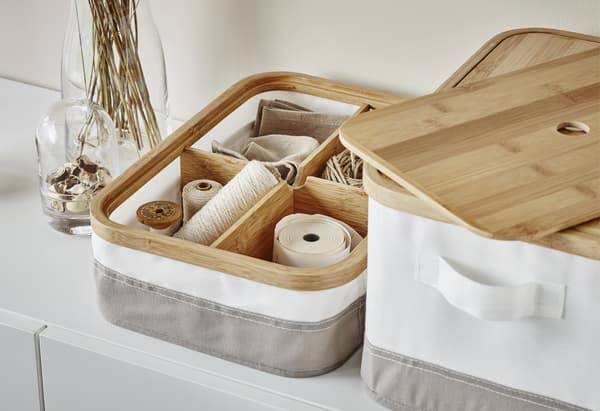 Gros plan de boîtes blanches et grises avec couvercle en bois, avec nécessaire de couture rangé dans les compartiments intérieurs en bois.