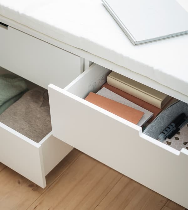 Gros plan de deux commodes NORDLI blanches ouvertes, dans lesquelles sont rangés des livres et des vêtements