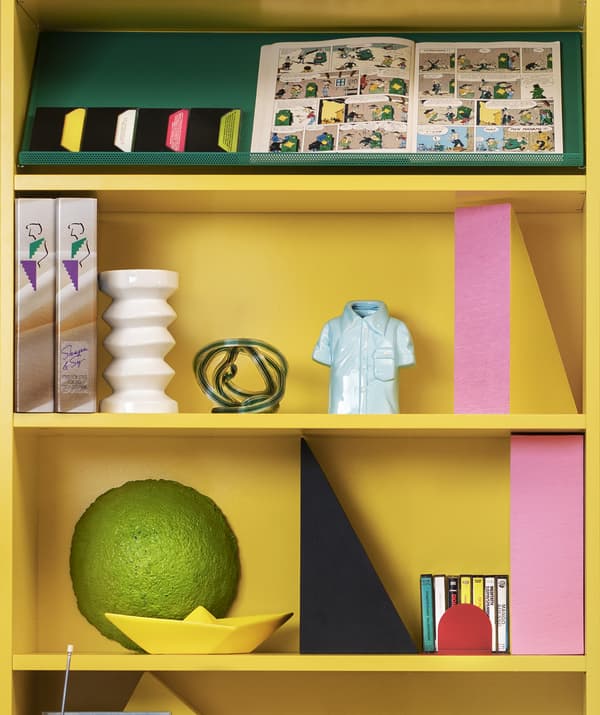 Gros plan de deux tablettes d’une bibliothèque jaune vif ornées d’objets décoratifs.