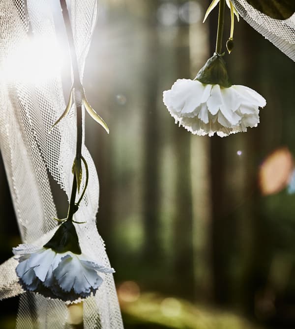 Gros plan de fleurs blanches artificielles et de bandelettes de voilages accrochées à une barre, pour la réalisation d’un photomaton de mariage