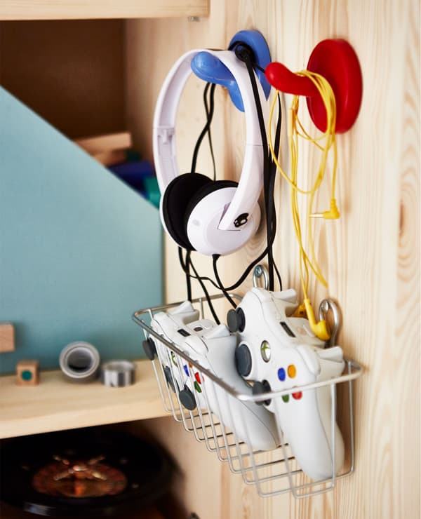 Gros plan de l’intérieur de la porte de l’armoire, avec crochets pour casques et panier métallique contenant les télécommandes.