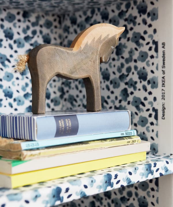 Gros plan de livres et d’un cheval comme objet de décoration sur une étagère au motif floral bleu.