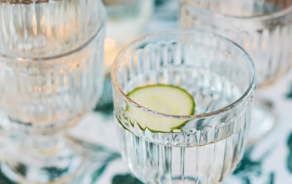 Gros plan de verres transparents remplis d’eau et une tranche de concombre dessus.