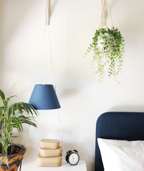 Gros plan du coin d’un lit et d’une table de chevet, avec de petites boîtes empilées et des plantes vertes.
