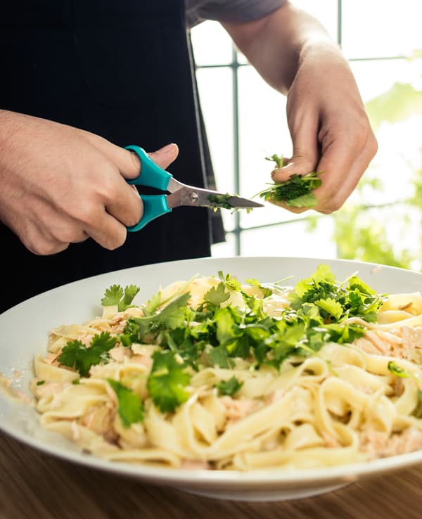 Gros plan d'un ado en train de ciseler de la coriandre sur des pâtes
