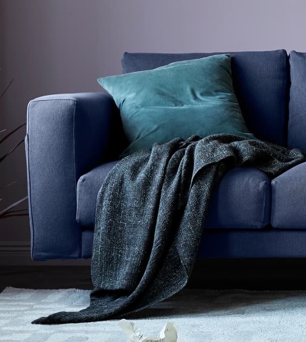 Gros plan d'un canapé gris avec plaid et coussin.