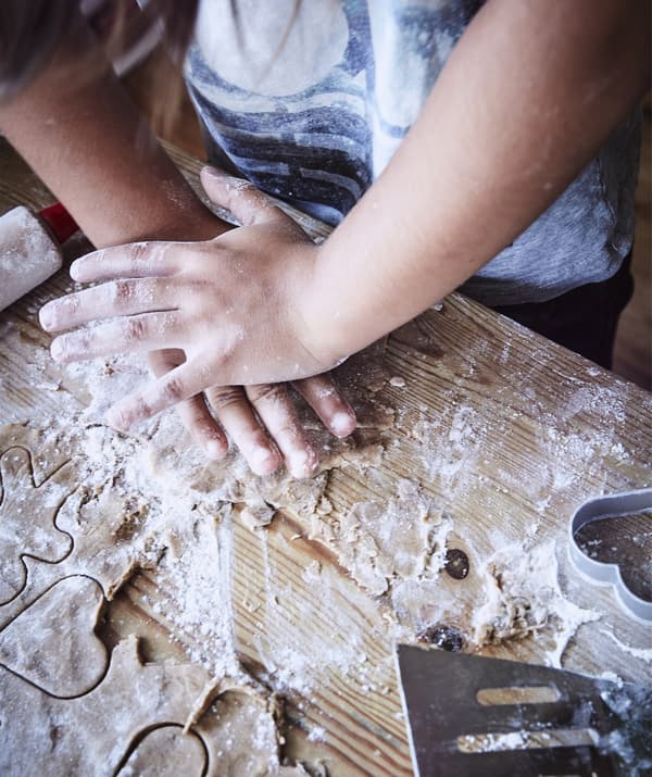 Gros plan d’un enfant découpant des formes dans la pâte sur un plan de travail enfariné.