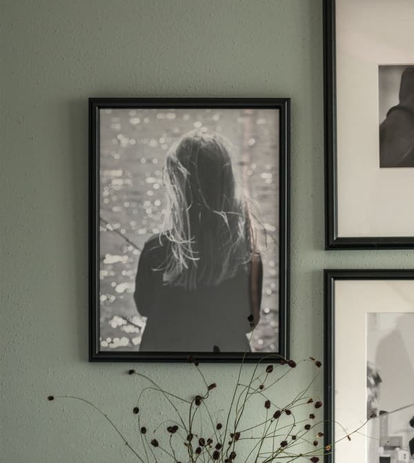 Gros plan d’un tableau sous cadre noir ornant un mur gris-vert.