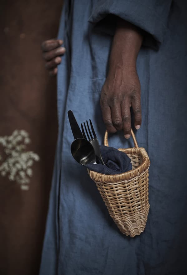 Gros plan d’une femme tenant un petit panier en rotin contenant des couverts.