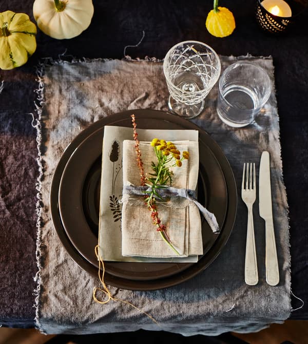 Gros plan d'une place à table décorée dans des teintes naturelles, avec des morceaux de lin teint et de petites courges décoratives.
