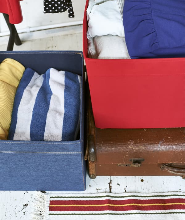 Gros plan sur des vêtements dans une boîte en denim et une boîte rouge posée sur une valise.