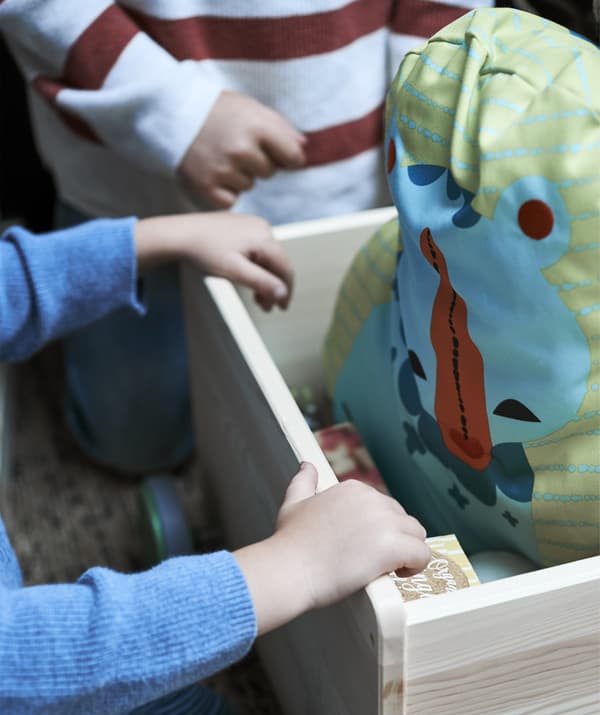 Gros plan sur les mains d’un enfant dans une caisse en bois avec une peluche à l’intérieur.