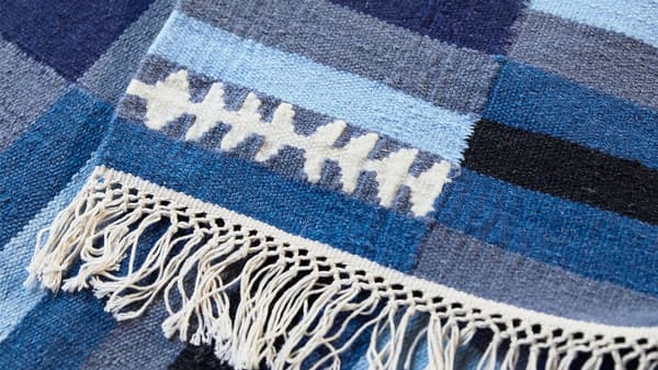 Gros plan sur un tapis en laine fait main TRANGET rayé blanc, noir, gris et bleu, avec des franges sur le bord.