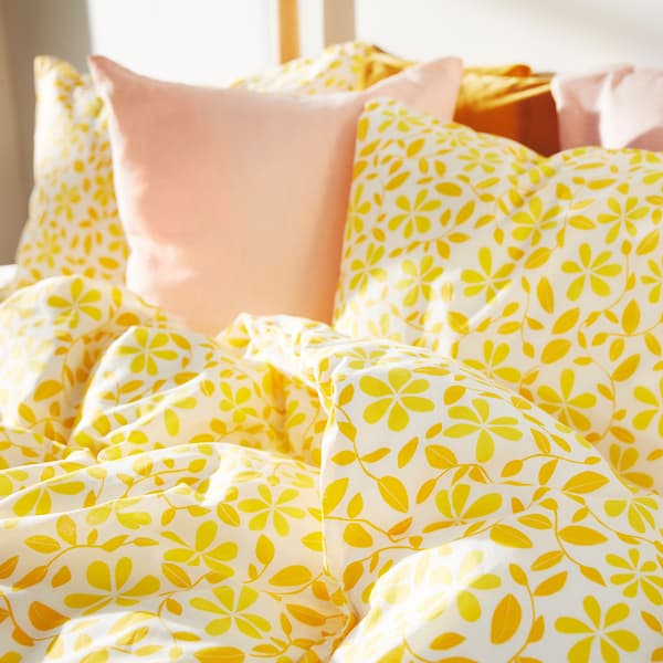 Gros plan sur une housse de couette à motif floral jaune vif et des coussins rose clair.