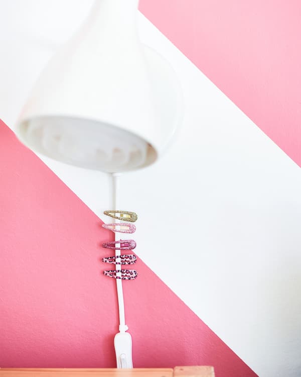 Gros plan sur une lampe de lecture fixée au mur, avec quelques pinces à cheveux attachées sur le fil pour plus de facilité.