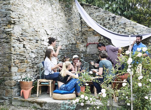 Groupe de personnes rassemblées prenant un verre sur la terrasse près du mur de pierre