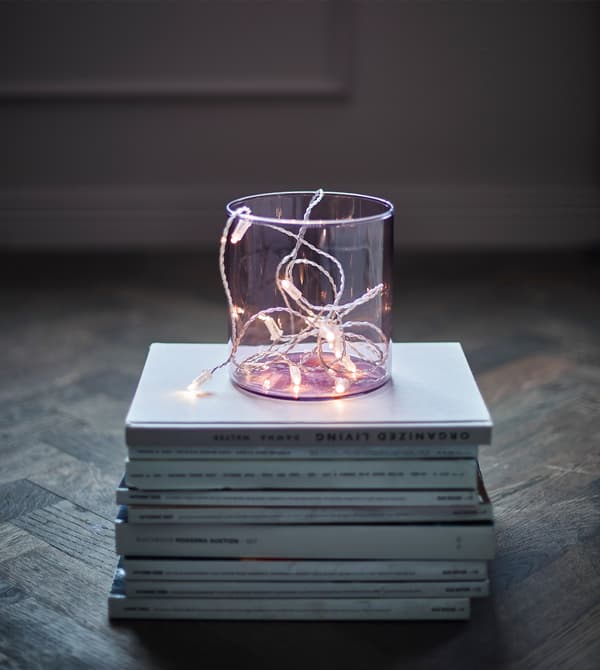 Guirlande lumineuse à LED dans un vase transparent posé sur une pile de magazines.