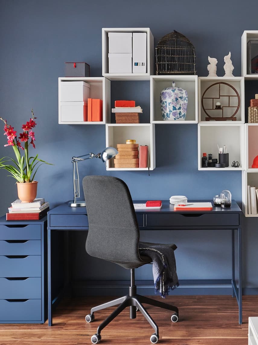 Habitación de color azul con repisas de color blanco colgadas en la pared, un escritorio de color azul y una silla de color negro.