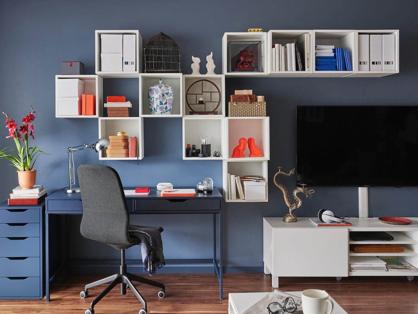 Habitación de color azul con un escritorio de color azul y repisas de color blanco. AL costado del escritorio se ve un rack de TV con un televisor encima.