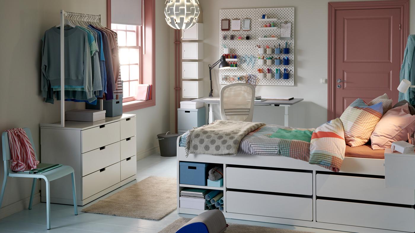 Habitación de estudiantes en colores pastel con una cama con un espacio de almacenaje integrado, un escritorio y un armario para colgar ropa cerca.