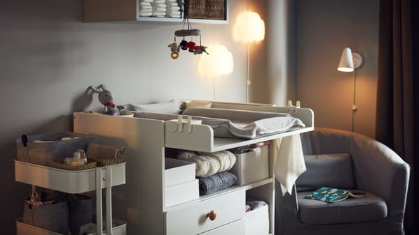 Habitación de un bebé con una cómoda blanca, un carrito y un sillón gris.
