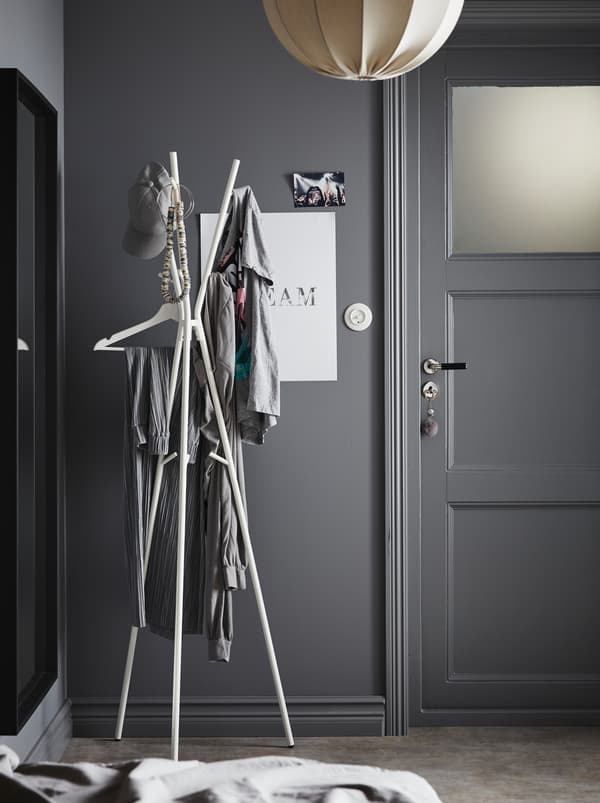 Hallway area in a gray color scheme. By the front door stands an EKRAR hat and coat stand, holding various garments.