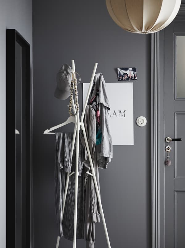 Hallway area in a grey colour scheme. By the front door stands an EKRAR hat and coat stand, holding various garments.