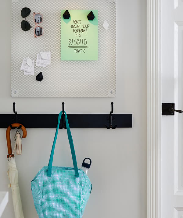 Hallway noticeboard with a remember-your-lunch note. A rack of hooks below, one holding a prepared lunch bag.