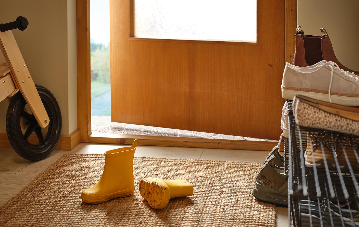 Hallway with a pair of children’s boots on the rug, filled shoe rack on the side, and a wooden kid's bike against the wall.
