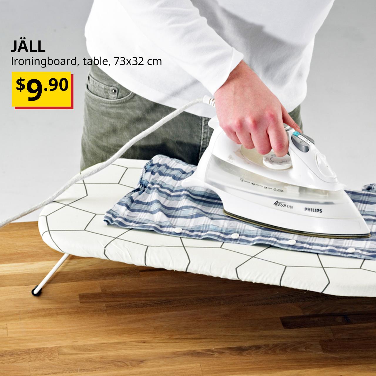 Hand holding a wired iron over a plaid t-shirt on JÄLL Ironingboard, table, 73x32 cm.