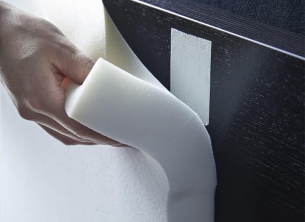 Hand holding some cut-foam paneling by a black-brown MALM bed frame.