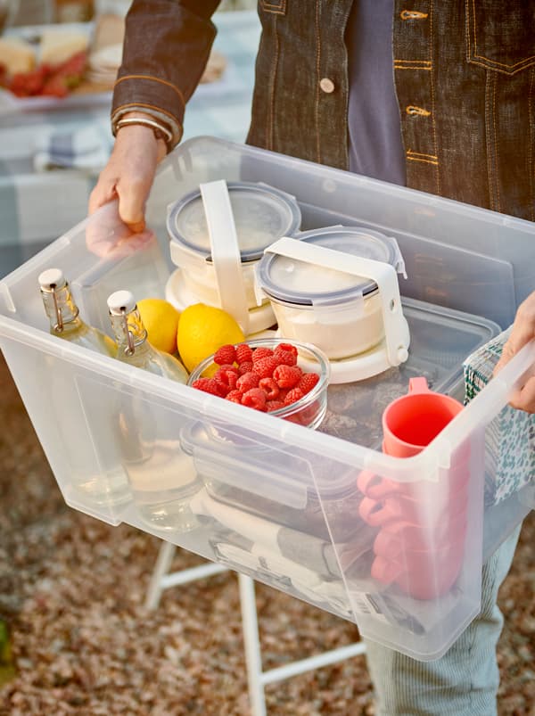 Hands holding a SAMLA box filled with tableware, glass bottles and food containers strapped to IKEA 365+ ice packs.