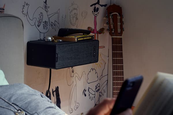 Haut-parleur étagère SYMFONISK noir fixé à un mur graffité dans une chambre à coucher. Une guitare est posée à proximité.