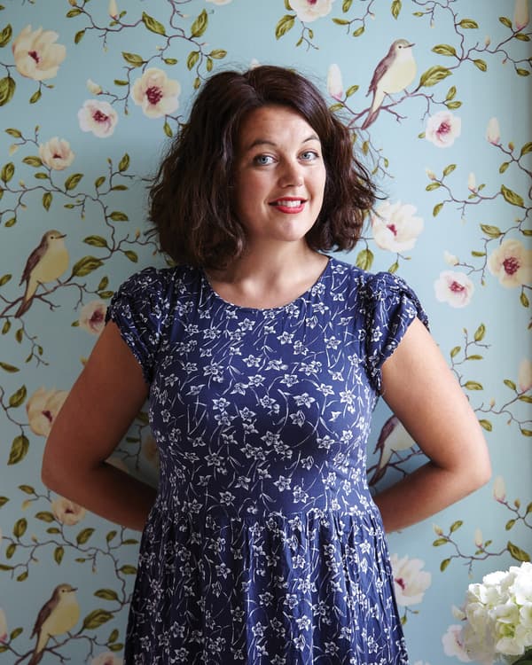 Helena stands against floral wallpaper.